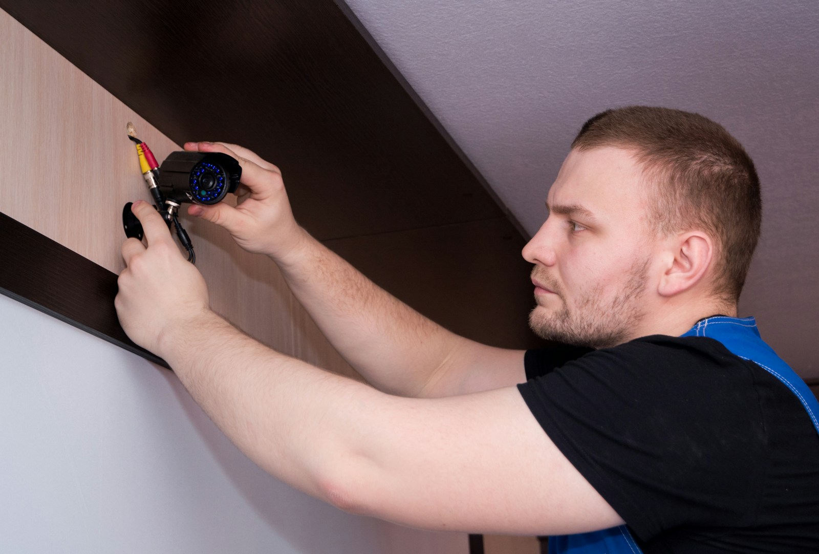 Technician mounting and wiring a security camera near the ceiling